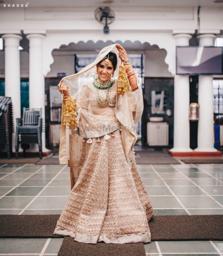 Photo of A Sikh bride posing in an off white and gold lehenga before her Anand Karaj ceremony