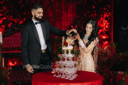 Photo of The couple pouring champagne in a champagne tower with the bride in a rose gold lehenga