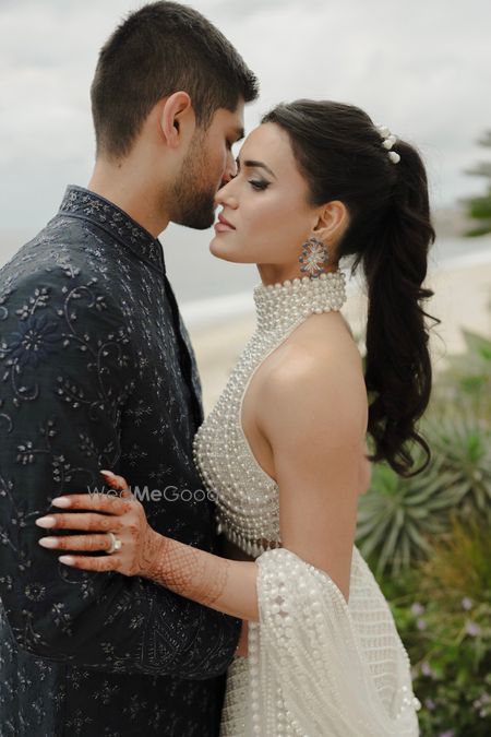 Photo of Couple shot from the sangeet with the bride in a stunning pearl work halter neck blouse and high ponytail
