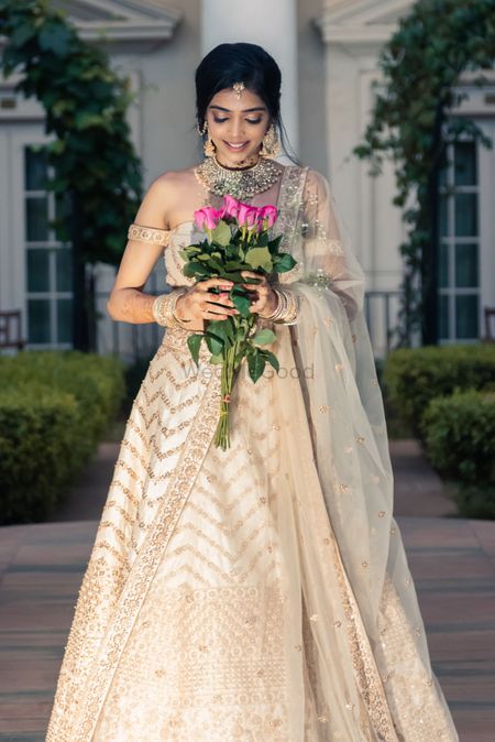 A bride in an ivory and gold lehenga with off-shoulder blouse and gold jewellery