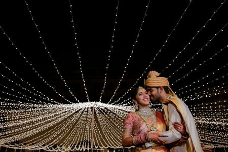 Couple posing under a sky of fairy lights.