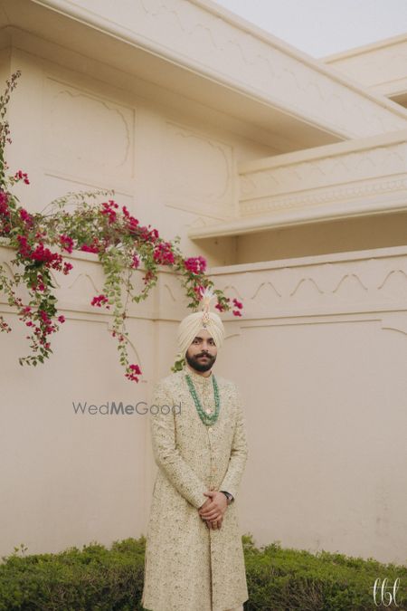 Photo of Lovely sage green sherwani with monotone work and contrasting emerald jewellery for the groom