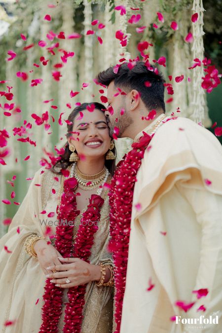 Candid capture of the bride and groom sharing a kiss just after the jaimala ceremony in gold outfits