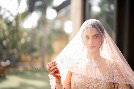 Lovely veil shot of the bride in a lace and shimmer pastel peach lehenga