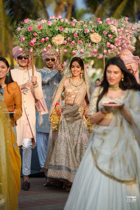 Photo of A bride ina  pink lehenga entering under a phoolon ki chadar