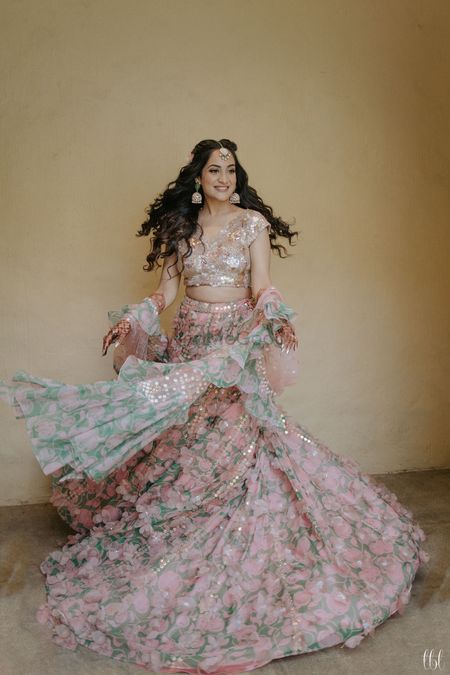 bride twirling in light pink mehendi lehenga with ruffled dupatta