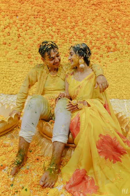 Photo of happy haldi couple shot against floral wall backdrop