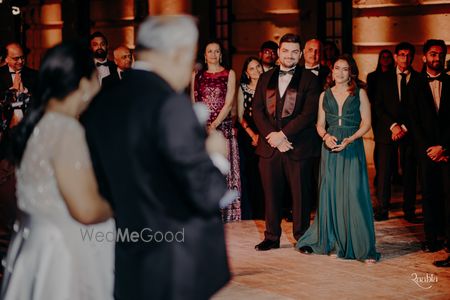 Photo of Candid capture of the bride and groom as they look to the father of the bride giving a speech