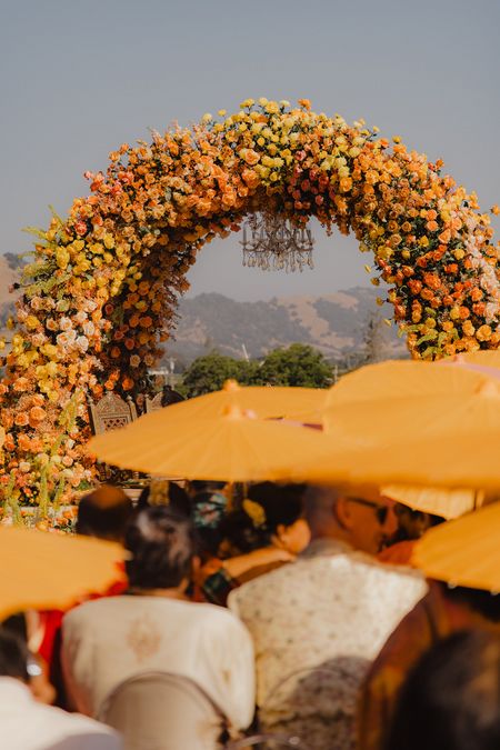 Photo of Glorious outdoor mandap in an arch style with lovely bright orange and yellow flowers