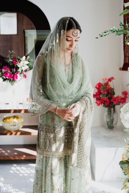 A coy bride to be at her roka ceremony, dressed in a pastel green sharara