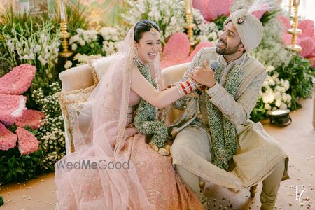 Fun candid capture of the bride and groom on the wedding day with bride in a peach lehenga and groom in a sage green sherwani