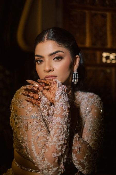 Photo of Stunning bridal look with nude makeup and a sheer outfit with lace style detailing on the hands