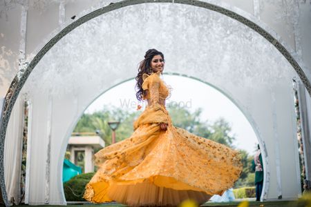 Photo of Bride twirling in yellow mehendi lehenga with ruffled blouse