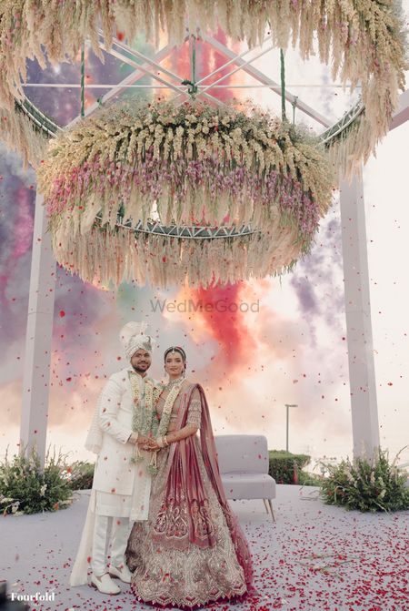 Photo of Stunning shot of the just married couple against the floral mandap and smoke bombs in the background