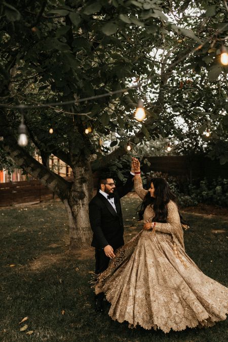 Photo of couple on reception with bride twirling in golden lehenga