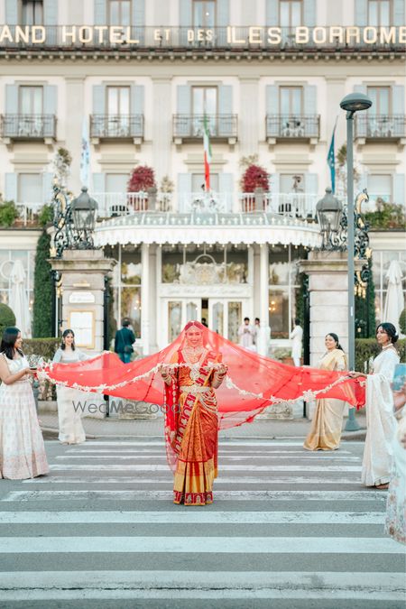 Grand bridal entry in a red saree and her bridesmaids holding the veil on the wedding day