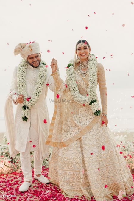 Fun couple photograph of a just married moment with the bride in nude and white lehenga and groom in white sherwani
