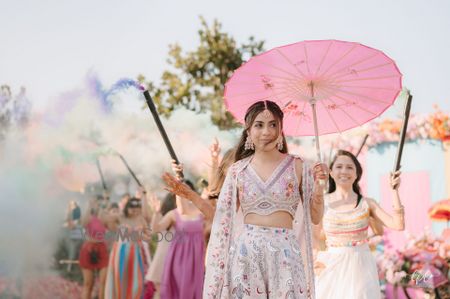 Beautiful shot of the bride entering with her bridesmaids on the mehendi day under pink parasols and colourful smokebombs