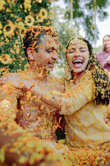 Fun haldi photo of the bride and groom in yellow outfits and a yellow flower shower