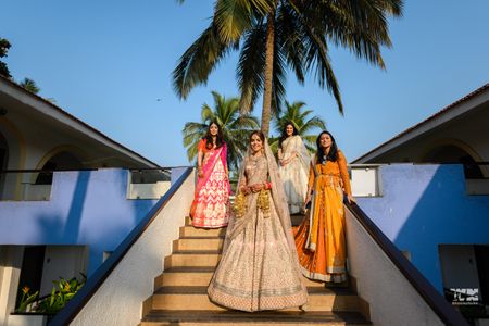 Photo of A bride in a light pink lehenga poses with her bridesmaids on her wedding day