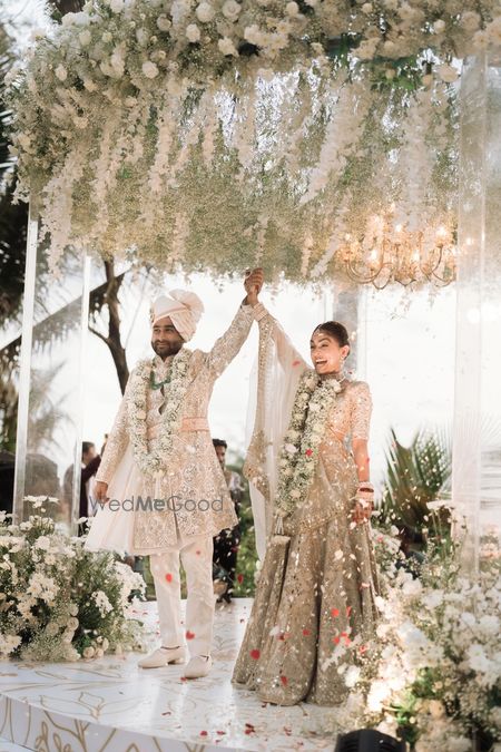 Just married couple shot with couple in white outfits and an outdoor mandap with florals