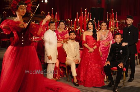 Photo of Family portrait with the bride in a stunning strapless lehenga in all red and open hair and the groom in an ivory sherwani for their reception event