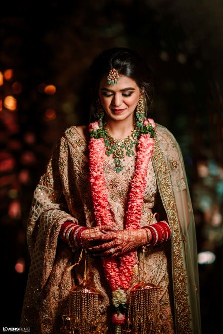 Bride wearing a pastel pink lehenga with emerald jewellery.