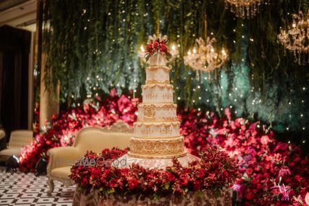 Photo of Stunning 5-tiered white and gold wedding cake with a floral decor table.