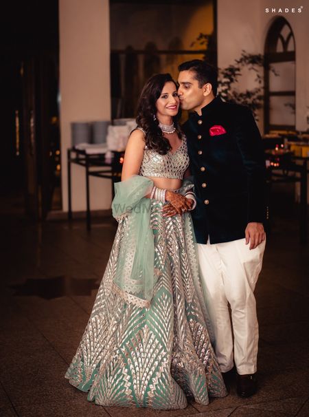 A bride in a shimmer lehenga posing with her groom-to-be at their sangeet