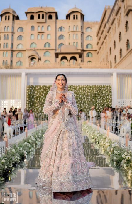 Beautiful bridal entry shot with aisle lined with floral decor and a pink lehenga