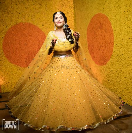 Photo of A bride twirling in a yellow lehenga in front of a wall decorated with marigold flowers