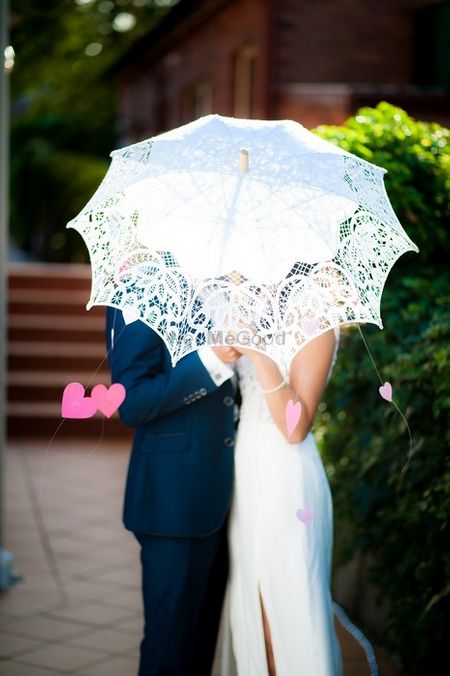 Photo of pre wedding shoot with lace umbrella and hanging pink paper hearts swishing through the wind