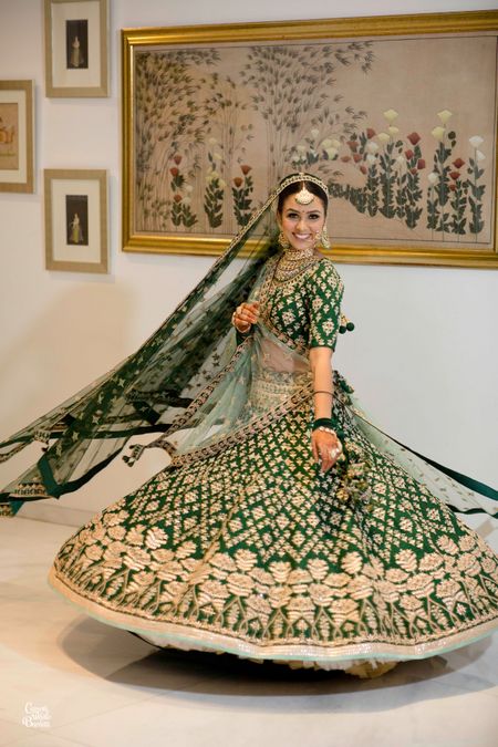 Photo of A bride in a dark green and gold lehenga twirling
