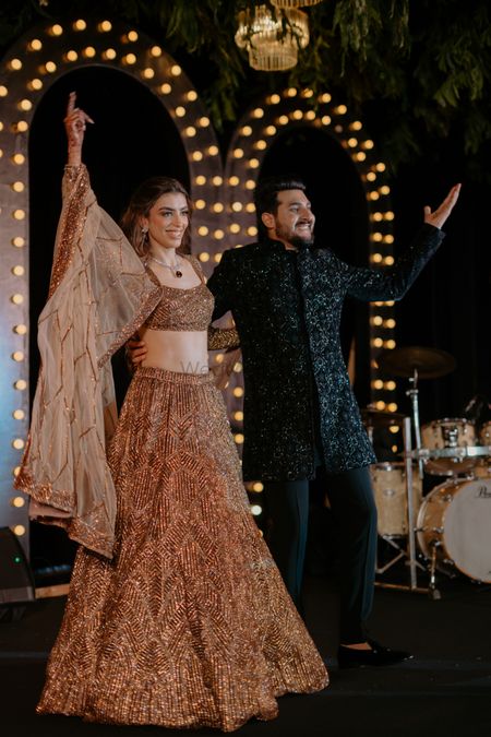 Photo of Candid capture of the bride and groom as they take on the stage in a champagne gold lehenga and black sherwani