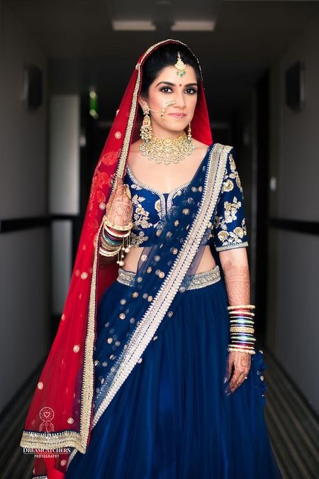Photo of Offbeat bridal lehenga with blue dupatta and red on head