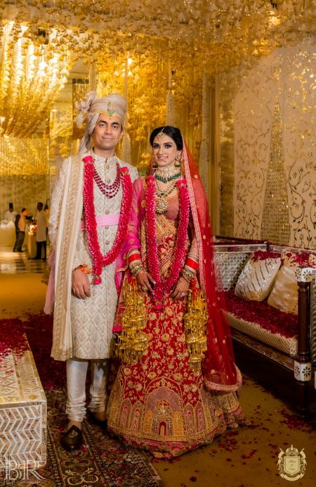 Photo of contrasting bride and groom outfits with both wearing red jaimalas