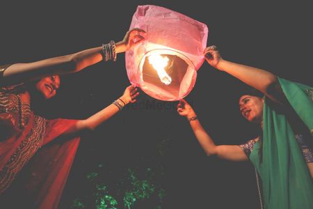 Photo of Releasing  paper lanterns into night sky whhile the couple sits on the feras