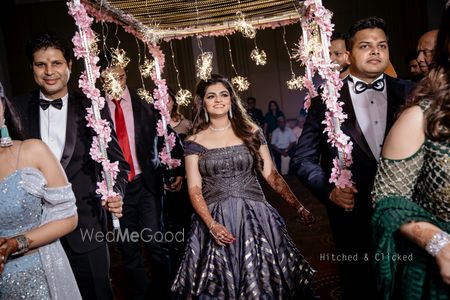 A bride dressed in grey gown entering under a unique phoolon ki chadar