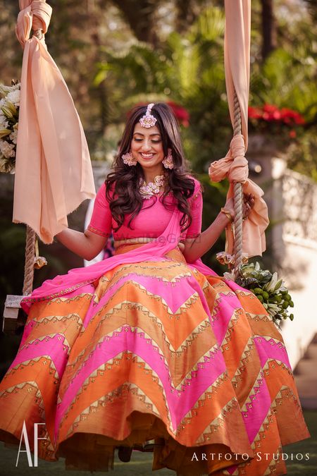 Photo of Bride on swing in orange and pink lehenga