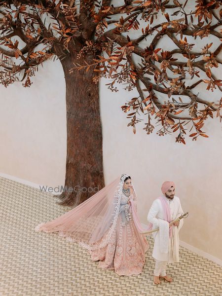 Couple taking pheras under a tree of life mandap in peach and white themed lehenga and sherwani