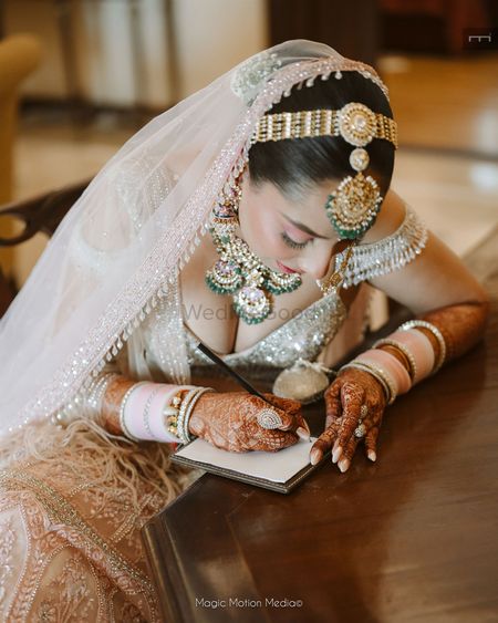 The bride writing her vows on her wedding day with a baby pink chooda in her hand