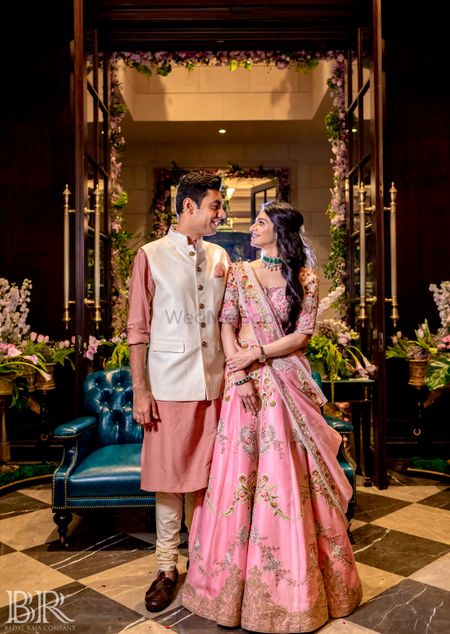 Photo of bride and groom in light pink outfits on mehendi