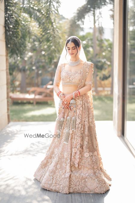 Bride in a gorgeous pastel peach lehenga in lace with diamond jewellery and matching kaleeras