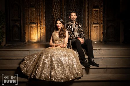 Photo of Glam couple portrait with bride in an all gold lehenga and groom in a black and gold sherwani