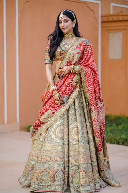 Bride wearing a heavy lehenga with a red bandhani dupatta.