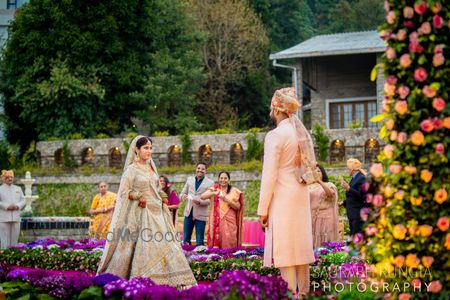 A bride in a light blue and gold lehenga walking towards her groom 