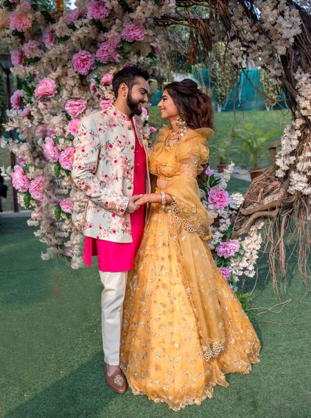 Mehendi couple portrait with groom in bright outfit and bride in yellow lehenga 
