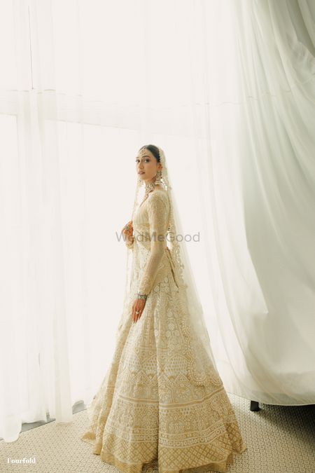 Photo of Classic bridal portrait with the bride in a full sleeves blouse and white and gold lehenga on the wedding day