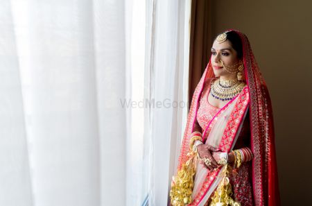 Photo of A bride in a red lehenga with gold kalire posing on her wedding day
