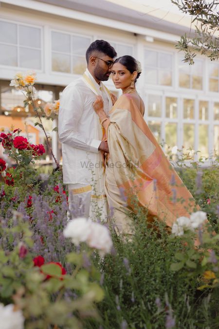 Lovely couple portrait in a field of flowers with the bride in a offwhite pastel silk saree